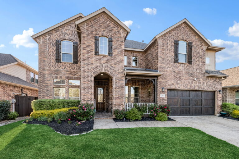 a two story brick house with attached garage and well maintained front yard