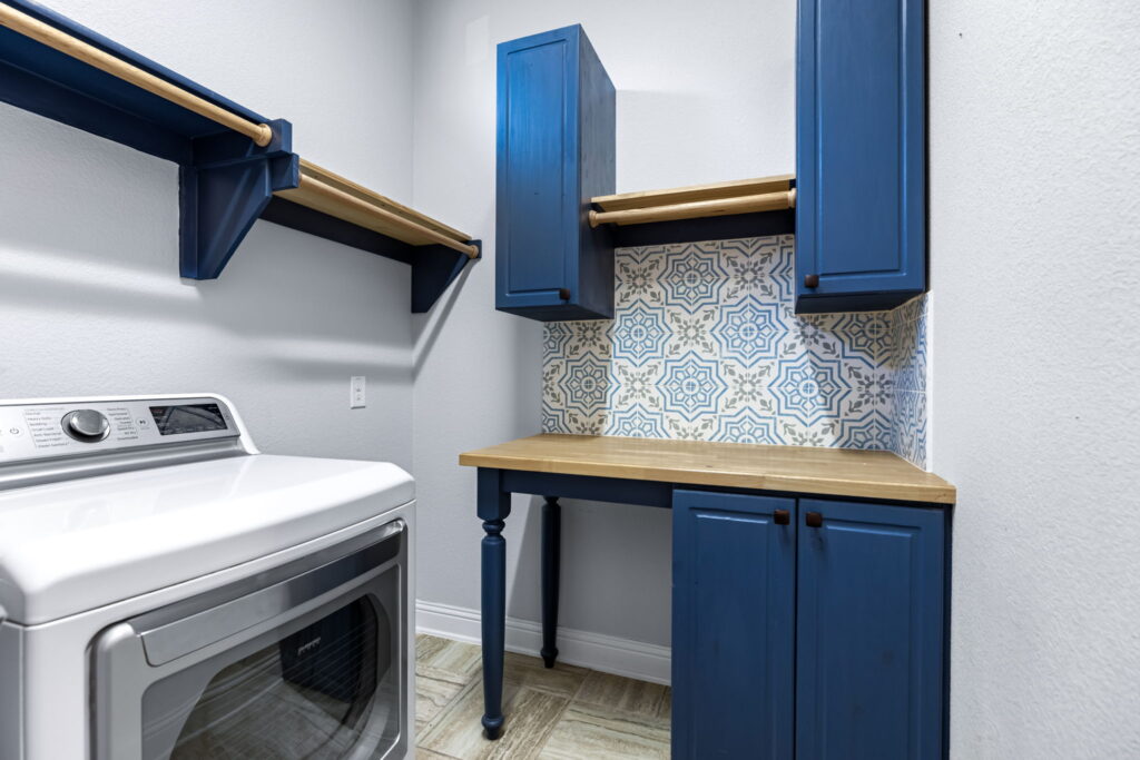 a laundry room features bold blue cabinets paired with a natural wood countertop and decorative tile backsplash