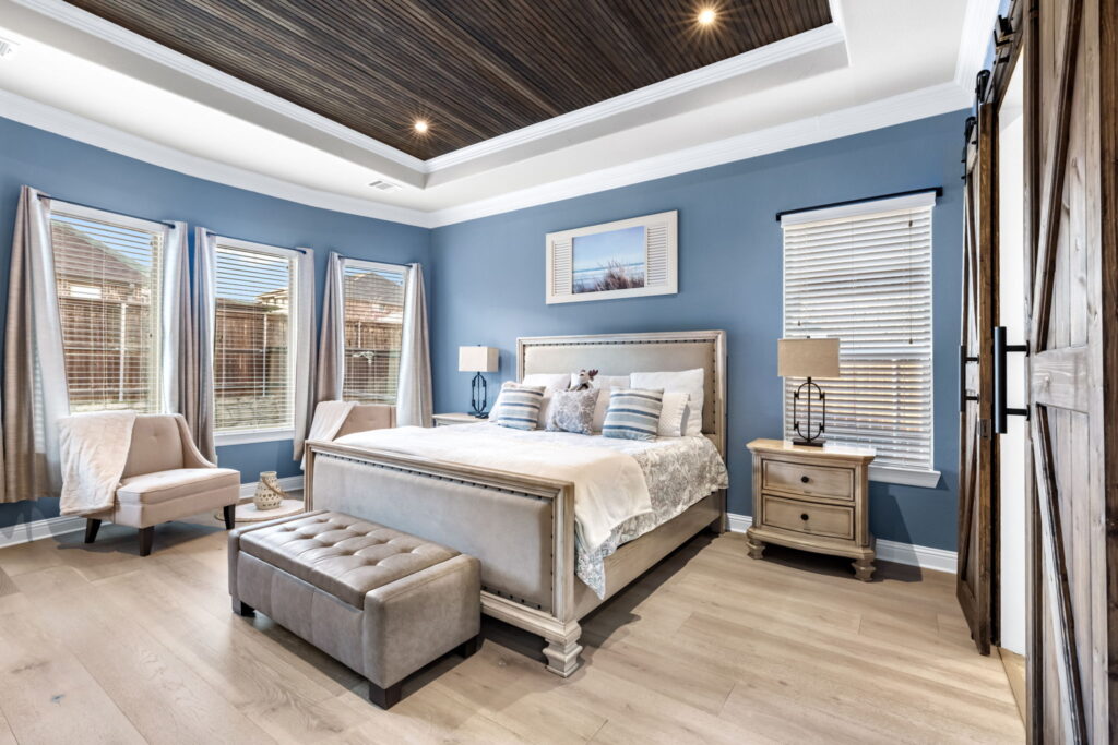 Modern bedroom with blue walls, a light wood-slat tray ceiling, and sliding barn doors.