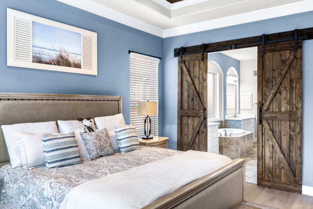 Modern bedroom with blue walls, a light wood-slat tray ceiling, and sliding barn doors.