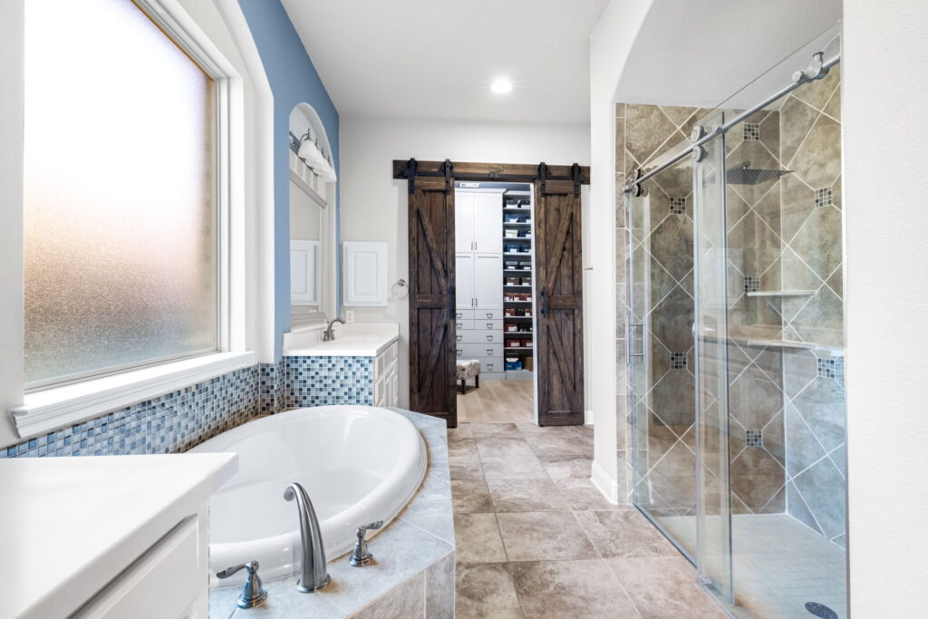 a primary bathroom featuring a white vanity with a large mirror and a separate bathtub