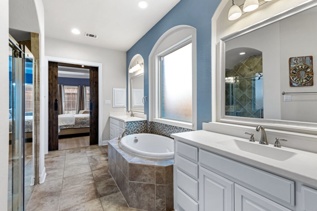a primary bathroom featuring a white vanity with a large mirror, a separate bathtub