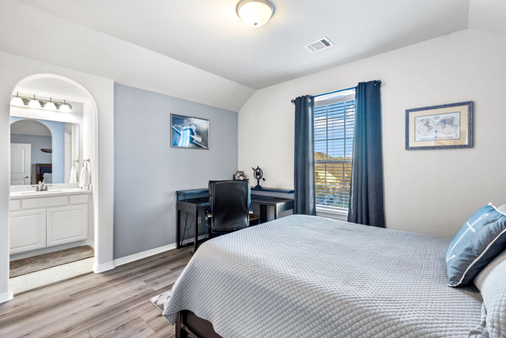A spacious bedroom with light gray walls, dark wood furniture, wood-look flooring, and a patterned accent chair in the corner.