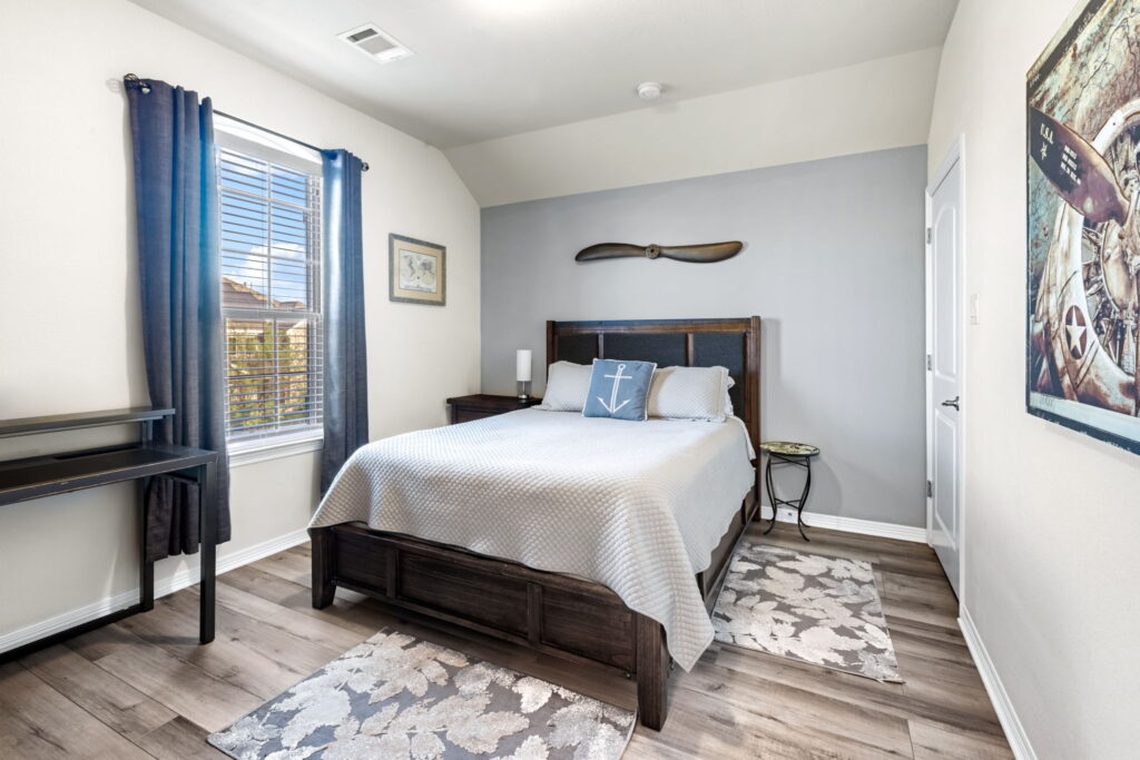 A spacious bedroom with light gray walls, dark wood furniture, wood-look flooring, and a patterned accent chair in the corner.
